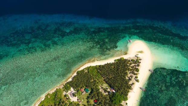 The island of white sand on a large atoll, view from above. Tropical island with palm trees. Seascape with a paradise island. Digyo Island, Philippines. Summer vacation and tropical beach concept.