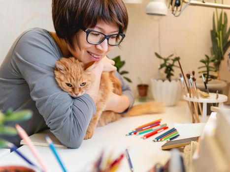 Woman with short hair cut hugs cute ginger cat. Fluffy pet and artist. Calming hobby, anti stress leisure.