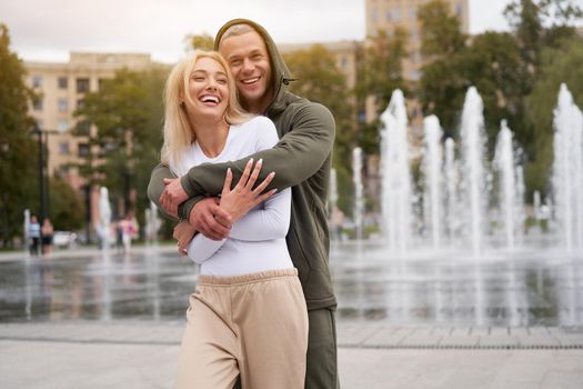 Couple in love walking outdoors park fountain Caucasian man woman walk outside after jogging dressed sport clothes Healthy livestyle dress up the hood
