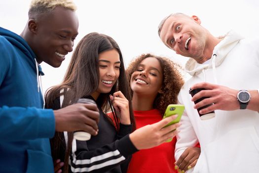 Multi-ethnic group teenage friends looking smartphone screen. African-american asian caucasian student spending time together Multiracial friendship Smiling People colorful sportswear drink coffee