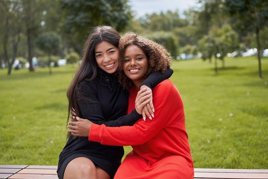 Diversity and feminity concept. Happy smiling Confident young mixed race women sitting bench park outdoor Asian and african american female resting on nature summer day