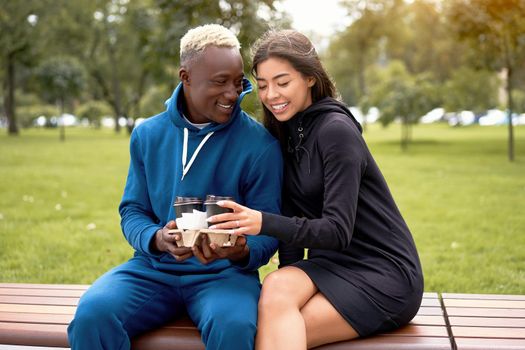 African american man proposes coffee asian woman Multiethnic friendship. Interracial relationship Young adult international couple drink hot beverage spending time together outdoor bench park Summer