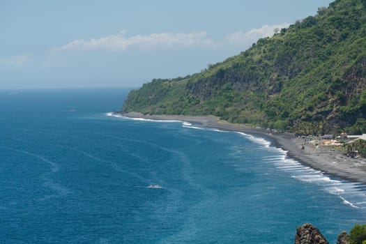 Rocky coast with high cliffs, sea coast, ocean, mountains, sea, beach, sky, clouds. Bali, sea surf with breaking waves on the coast, Indonesia. Ocean with waves and rocky cliff.