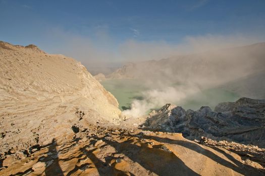 Crater with acidic crater lake, Kawah Ijen the famous tourist attraction, where sulfur is mined. Extraction of sulfur in the crater of a volcano. Sulfur gas, smoke.