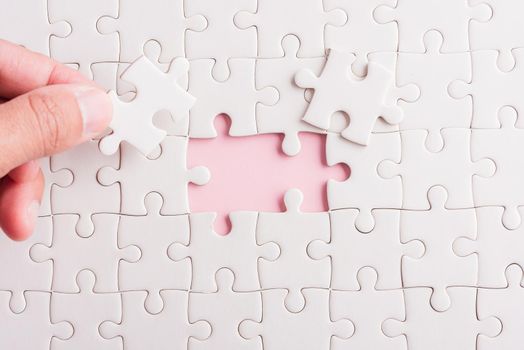 Top view flat lay of hand-holding last piece white paper jigsaw puzzle game last pieces put to place for solve problem complete mission, studio shot on a pink background, quiz calculation concept