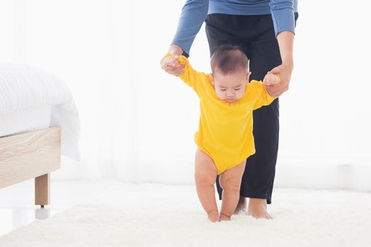 Asian little baby taking first steps learning to walk with mother help support the cute unstable walking toddler. Happy family first steps parenthood concept