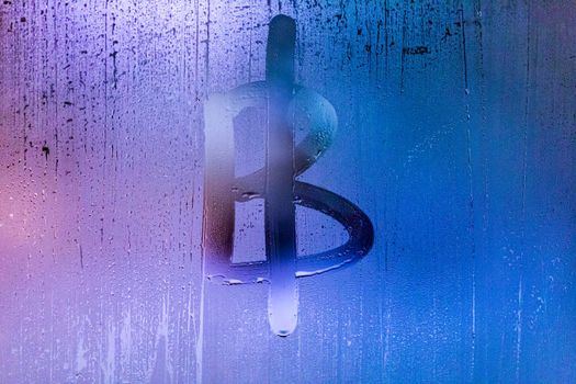 bitcoin symbol - handwritten on wet glass of night window, close-up with selective focus and background blur