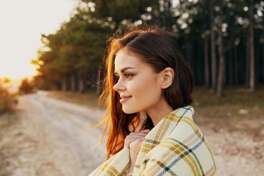 Happy woman with a warm blanket on her shoulders near the forest in nature and the road. High quality photo