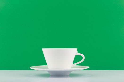 White tea cup against green background with copy space. Concept of green, organic, natural or herbal tea, wellbeing and healthy life style