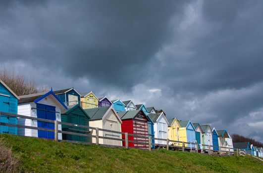 Colourful beach huts, English beach resort. Seaside beach chalets, famous brightly painted Beach Huts. UK Seaside and holiday locations. Summer sea side landscape with grass, huts, sky