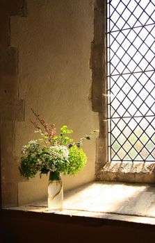 Old Christian church interior with sun rays from the window on flowers bouquet. Religion, old architecture, Christianity, travel, belief concept