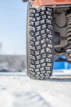 Car wheel on snow in winter close-up. The suspension and chassis of the car are visible. The car is parked in a snowy parking lot.