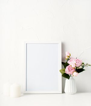 Mock up white frame on the wall with peonies and white candles
