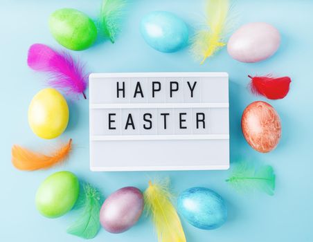 Easter holiday. Top view Happy Easter light box decorated with bright colored eggs and feathers