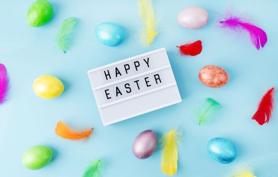 Easter holiday. Top view Happy Easter light box decorated with bright colored eggs and feathers