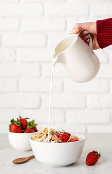 Healthy eating and dieting. Female hand pouring milk to breakfast cereal bowl on white brick wall background
