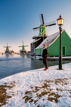 young man walked in the snow, snow covered windmill village in the Zaanse Schans Netherlands, historical wooden windmills in winter Zaanse Schans Holland during winter