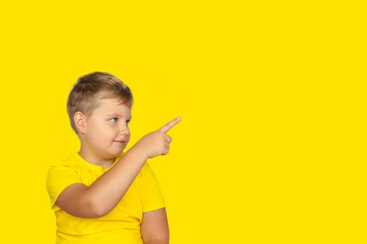 A boy in a yellow T-shirt on a yellow background points his fingers at something. The concept of a banner with information. Space for the text. Concepts