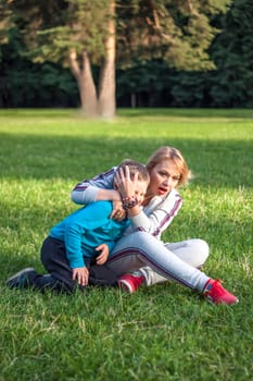 A girl plays with her son on a green lawn. Live emotions of mother and son. Family.