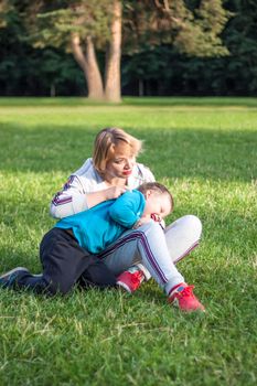 A girl plays with her son on a green lawn. Live emotions of mother and son. Family.