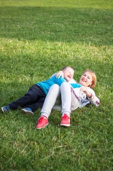 A girl plays with her son on a green lawn. Live emotions of mother and son. Family.