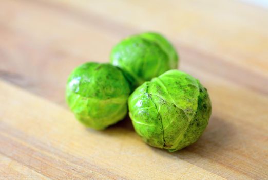 Group of three whole fresh brussels sprouts on wooden plate.