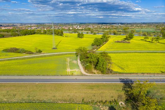 Aerial drone look to long highway between yellow fields of colza at cloudy sunny day