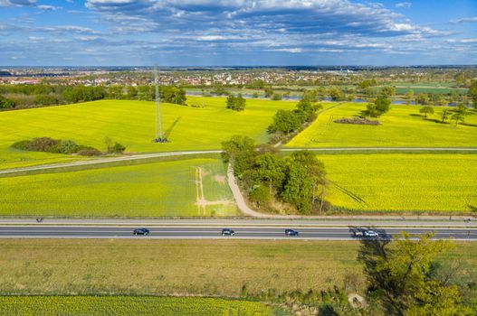 Aerial drone look to long highway between yellow fields of colza at cloudy sunny day