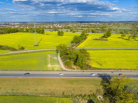 Aerial drone look to long highway between yellow fields of colza at cloudy sunny day