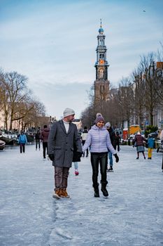 couple visit Amsterdam during Winter with people Ice skating on the canals in Amsterdam the Netherlands in winter, frozen canals in Amsterdam during winter. 