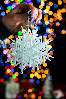 Holding Christmas snowflake decoration isolated on background with blurred lights. December season, Christmas composition.