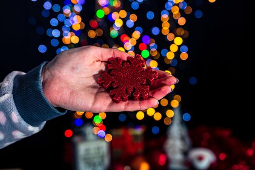 Holding Christmas snowflake decoration isolated on background with blurred lights. December season, Christmas composition.