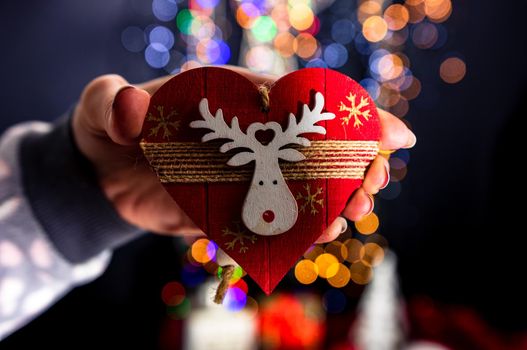 Holding Christmas heart shape decoration isolated on background with blurred lights. December season, Christmas composition.