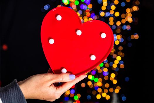 Holding Christmas heart shape decoration isolated on background with blurred lights. December season, Christmas composition.