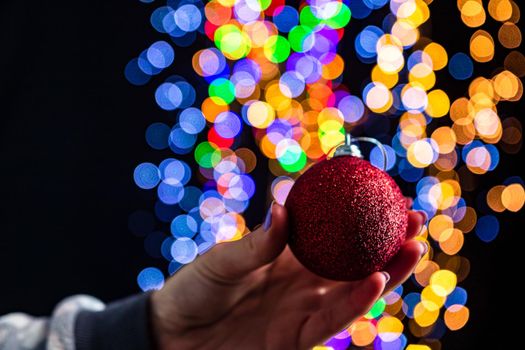 Holding Christmas bauble decoration isolated on background with blurred lights. December season, Christmas composition.