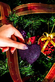 Hand putting heart shaped Christmas decorations on fir branches decorating Christmas tree, Christmas hanging decorations.