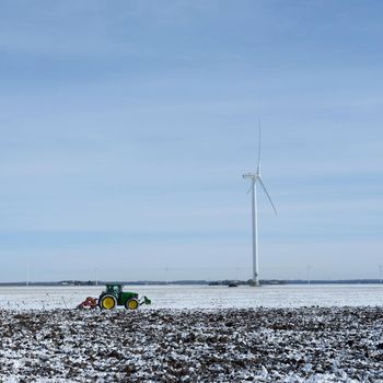 snow covered fields and tractor in dutch polder of flevoland under blue sky in winter