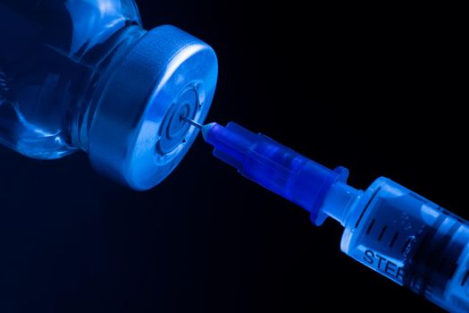 The drug is drawn into a syringe. Vaccine bottle. Medical chemical preparation and syringe under ultraviolet light. Narcotic drug.
