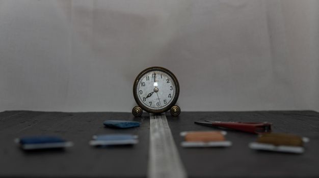 Clock surrounded by sewing utensils such as needle, thread and sewing tape measure.