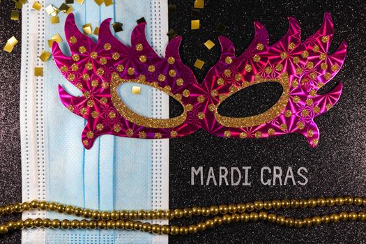 Mardi Gras carnival theme pink party mask with medical facemask and bead string layout on textured black