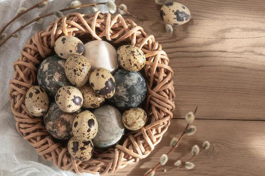 Easter composition - Easter eggs painted with natural dyes in a wicker nest on a wooden table, copyspace.