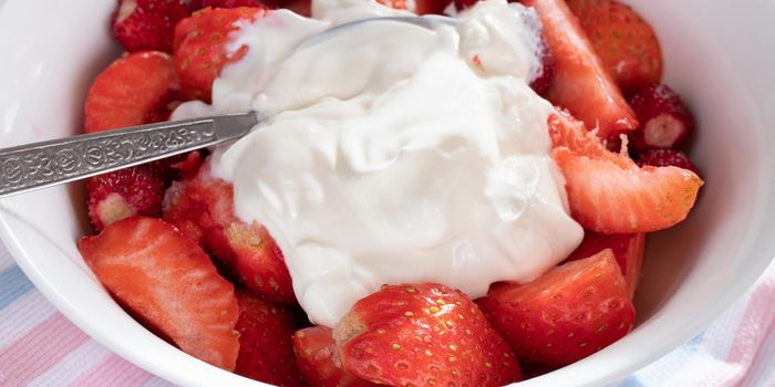 Natural sliced ripe strawberries in a white bowl with sour cream close up.