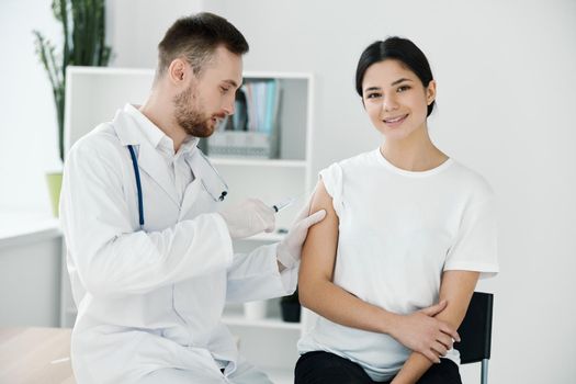 the doctor injects the covid-19 vaccine into the shoulder of the patient in a white t-shirt on a light background. High quality photo