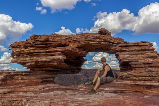 young man sitting in the Nature's Window, a natural arch rock formation in Kalbarri National Park on a sunny day, Western australia
