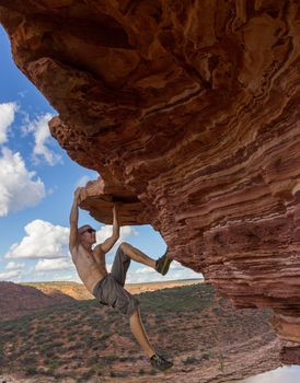Carefree man is climbing on red sandstone rock of Nature's Window in Kalbarri National Park