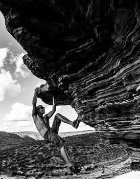 Sorgloser Mann klettert auf rotem Sandsteinfelsen des Naturfensters im Kalbarri-Nationalpark