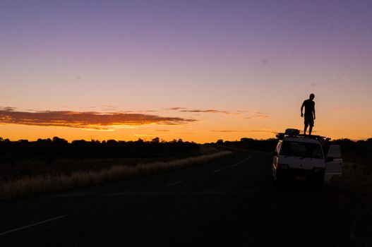 young man standing on car while a nice Sunset in the Outback of Australia