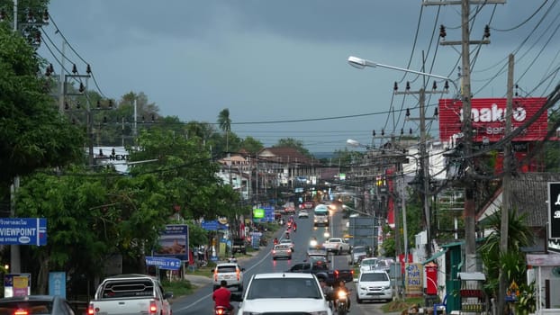 KOH SAMUI ISLAND, THAILAND - 11 JULY 2019 Busy transport populated city street in cloudy day. Typical street full of motorcycles and cars. Thick blue clouds before storm during wet season