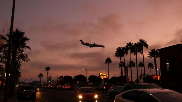 LOS ANGELES, CALIFORNIA, USA - 10 NOV 2019: Airplane landing, LAX airport. Passenger flight or cargo plane silhouette, dramatic pink sky. Aircraft arrival to airfield. International transport flying.