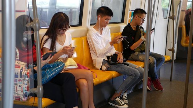 BANGKOK, THAILAND - 13 JULY, 2019: Asian passengers in train using smartphones. Thai people online surfing internet in bts car. Public transportation. Addiction from social media and phone in subway